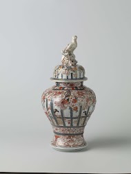 Balustervormige dekselpot met mensen in een interieur achter traliewerk, prunusbomen en bloemranken