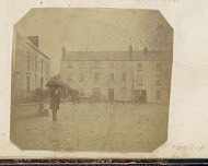 Man met een paraplu staand voor huizen, vermoedelijk in Birr