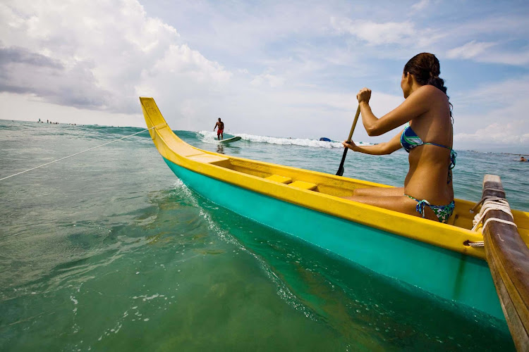 A young Hawaiian woman paddles an outrigger canoe. Hawaii is a mecca for water sports.