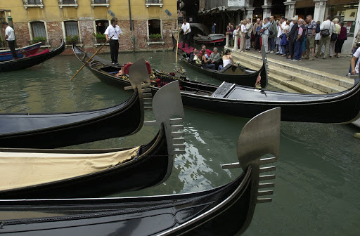 JFvenice-waitingroraride - One of the main gondola stations. Prepare to wait in line. The prongs on the ornaments, called ferros, on the boat's sterns represent the districts of  Venice.