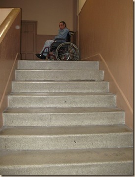 Escalera que da acceso al edificio que les ha sido concedido en cuya parte superior aparece Miguel en silla de ruedas, a quien Charo y otros compañeros tienen que subir y bajar a pulso cada vez que acude al centro