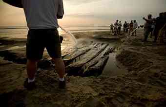 Volunteers and members of the North Carolina Wildlife Resources Commission use fire hoses, hand shovels and heavy equipment to remove the sand and pull what remains of a shipwreck off the beach in Corolla, N.C. on Tuesday, April 6, 2010. The wreck could be the oldest shipwreck on the Carolina coast. (L. Todd Spencer | The Virginian-Pilot) 