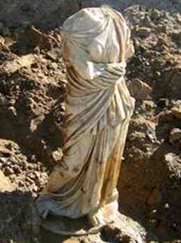 The white marble statue of a woman wearing a toga and sandals has no head or arms.