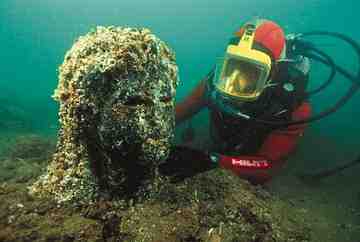 A diver is inspecting a Granite head emerging from the sediment at the Heracleion site. The head belongs to a statue of a Ptolemaic Queen dressed as the Goddess Isis.