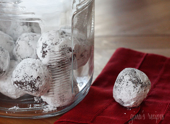Image shows powdered sugar chocolate cookies in a container, and one on a napkin next to it