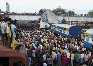 Onlookers stand at the site of a train accident at Sainthia in the eastern Indian state of West Bengal July 19, 2010. A speeding passenger train crashed into another waiting at a station in eastern India early on Monday, killing at least 60 people in India's second major accident in as many months, officials said. REUTERS/Stringer (INDIA - Tags: TRANSPORT DISASTER IMAGES OF THE DAY)