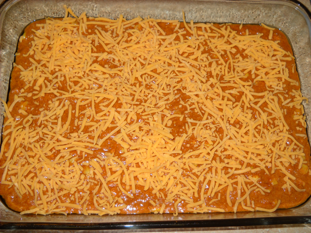 chili cheese cornbread mix in baking pan, topped with shredded cheese, ready to bake