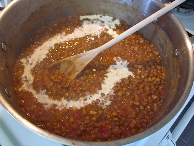 cream added to cooked lentil mixture in pot with wooden spoon 