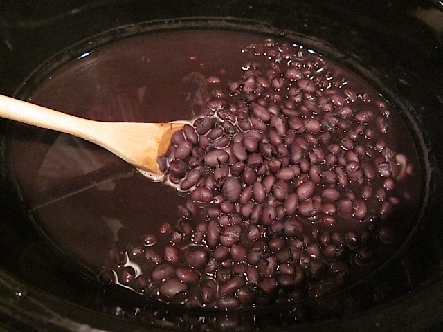 cooked black beans in pot with wooden spoon