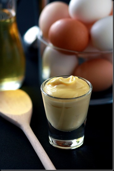 Homemade mayonnaise in a glass with a wooden spoon and eggs in the back. 