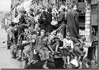 Oslo 8 mai 1945.  Den andre verdenskrig (1940-45) er over og frigjøringsfesten er igang i Oslo. Unge og gamle har besatt lastebiler av alle slag og kjører rundt i gatene. En norsk politimann har overtatt trafikkdirigeringen på Karl Johansgate mens en "slagen" tysk soldat bivåner det hele.SCANPIX/Arkiv.