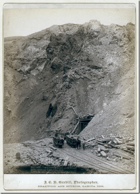 Title: Open cut in the great Homestake mine, at Lead City, Dak.
Distant view of mine entrance; four men posed on or near three mining cars on tracks. 1888.
Repository: Library of Congress Prints and Photographs Division Washington, D.C. 20540