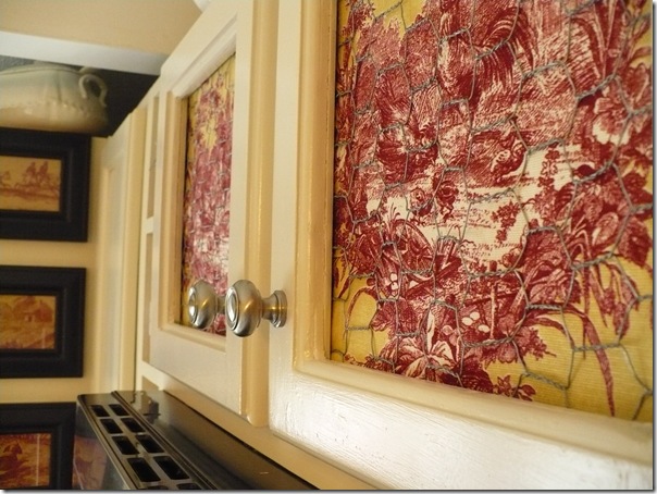 closeup of a kitchen cabinet with chicken wire and toile fabric