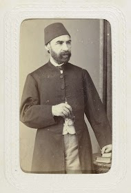 Studioportret van een man in lange jas met op zijn hoofd een fez