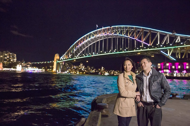 A couple takes in the Vivid Sydney Festival along Walsh Bay with the Sydney Harbour Bridge as a backdrop.