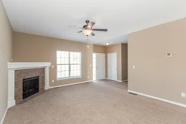 Living area with a tile fireplace in the left corner, a window, front door on the right, a ceiling fan, and tan color-scheme