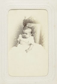 Studioportret van een baby in een witte jurk op een stoel