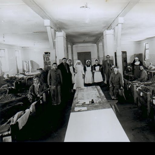 Former Auschwitz I. Hospital ward on the first floor of block 21, with the  Polish Red Cross nurses looking after the patients standing in the centre —  Google Arts & Culture