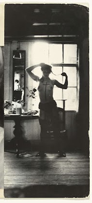 Halfnaakte vrouw met een kruis op haar borst getekend, staand voor een raam