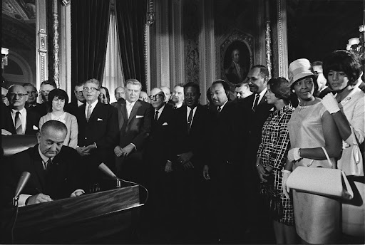President Lyndon B. Johnson signs the Voting Rights Act as Martin Luther King Jr. and other civil rights leaders look on